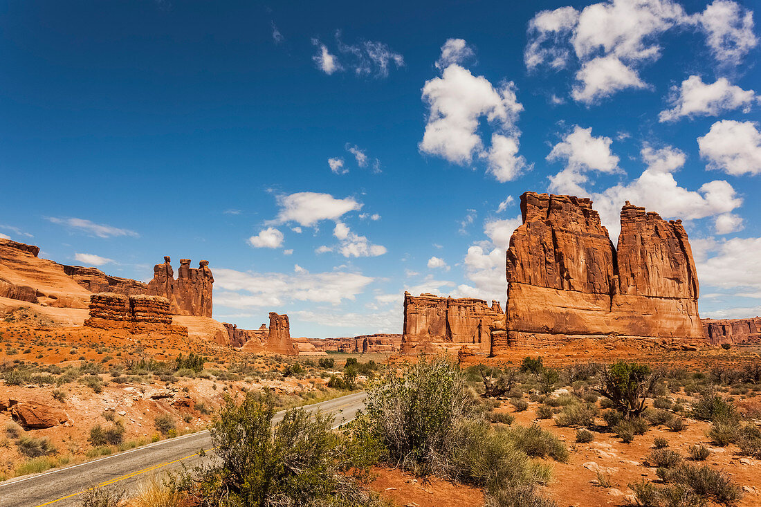 'Rugged rock formations and shrubs in the desert, with a road passing through; Arizona, United States of America'