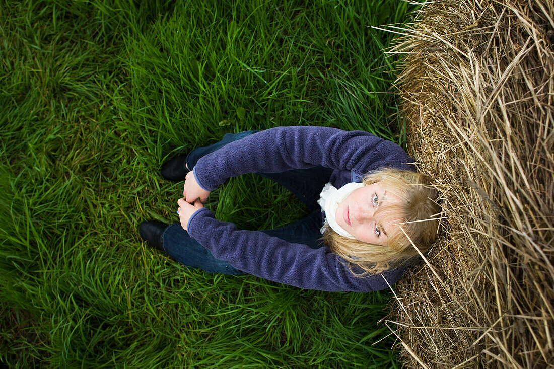 'High Angle View Portrait Of A Teenage Girl Sitting Against A Hay Bale; Homer, Alaska, United States Of America'