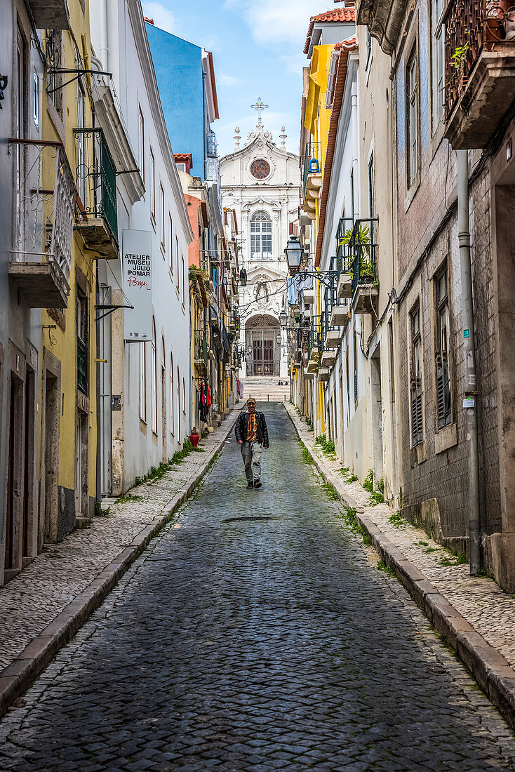 'Guy descending a narrow street with Igreja Paroquial das Merces in the background; Lisbon, Portugal'