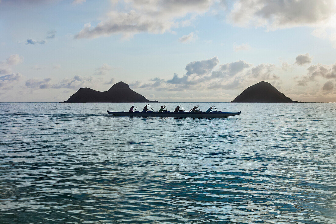 'A group of canoers paddling through Lanikai Beach in a canoe in front of the Mokulua islands, Kailua; Honolulu, Oahu, Hawaii, United States of America'