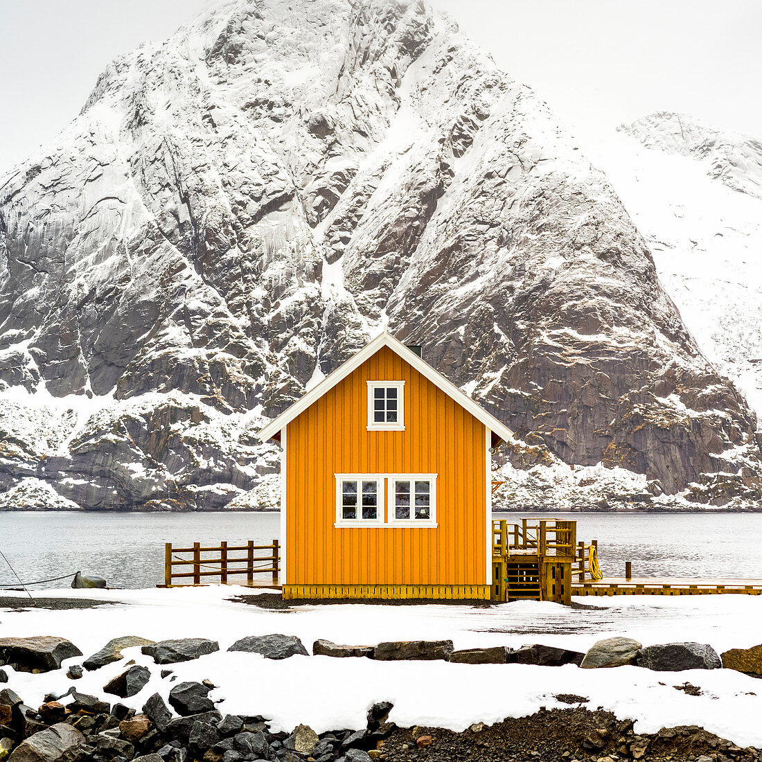 'Ein helles gelbes Gebäude am Wasserrand mit einem schneebedeckten Berg hinten; Nordland, Norwegen'