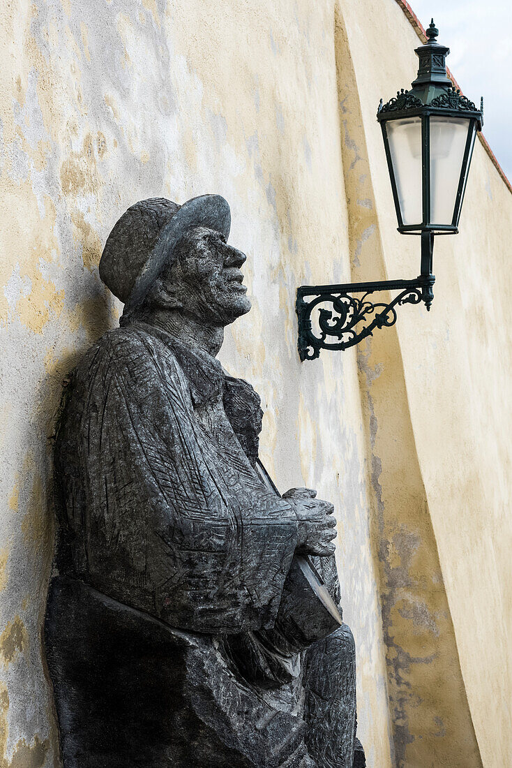 'Statue of a man leaning against a wall beside a light; Prague, Czech Republic'