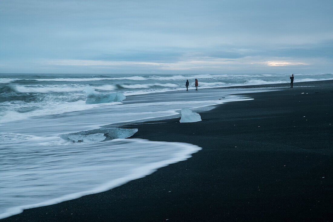 'People walking along the beach playing in the surf at Diamond Beach, South coast; Iceland'