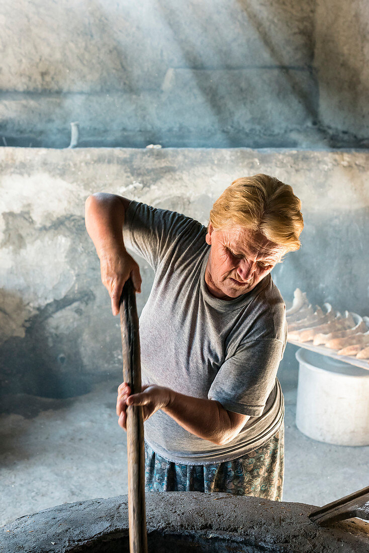 'Lokale Frau bereitet traditionelles Georgia-Brot unter den Strahlen des direkten Sonnenlichtes in einer inneren Oberfläche eines Ofens vor; Kakheti, Georgien'