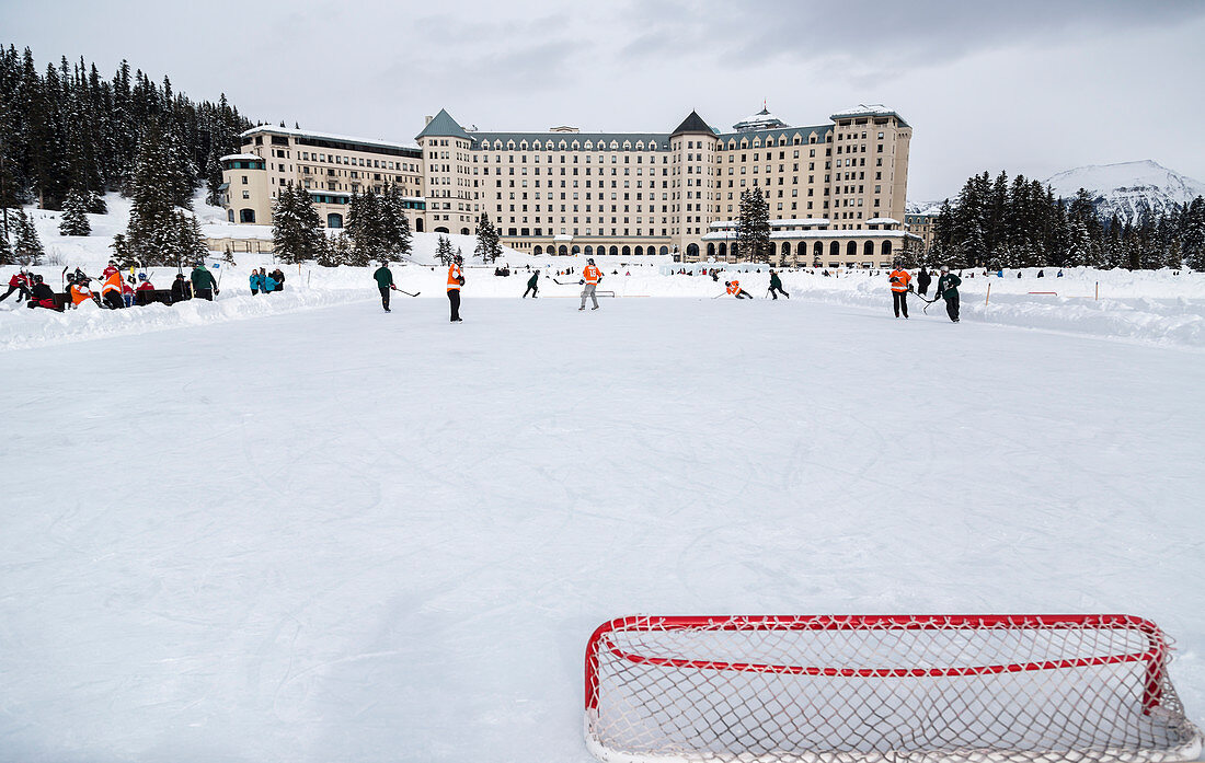 'A view from behind the hockey net during a pond hockey game in the winter on frozen Lake Louise in Banff National Park, against the background of the Fairmont Chateau Lake Louise Resort; Lake Louise, Alberta, CanadaEin Blick von hinter dem Hockey-Netz wä
