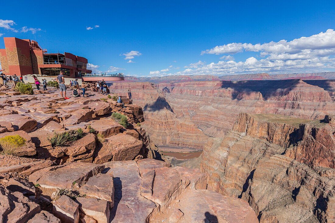 'The beautiful viewpoint at the West Grand Canyon Skywalk attraction, a group of tourists enjoys the skywalk while other tourists take photos on the edge of the canyon cliffs; Arizona, United States of America'