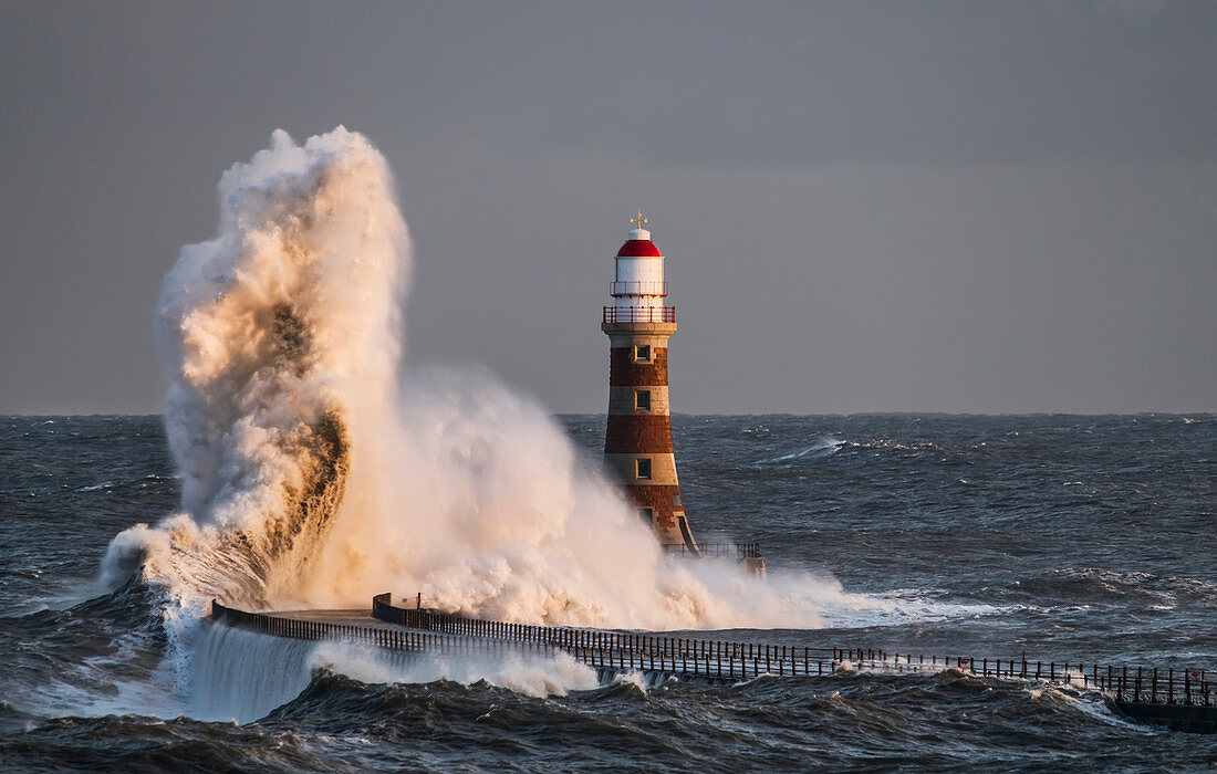 Wellen, die gegen Roker Leuchtturm am Ende eines Piers spritzen, Sunderland, Tyne und Wear, England
