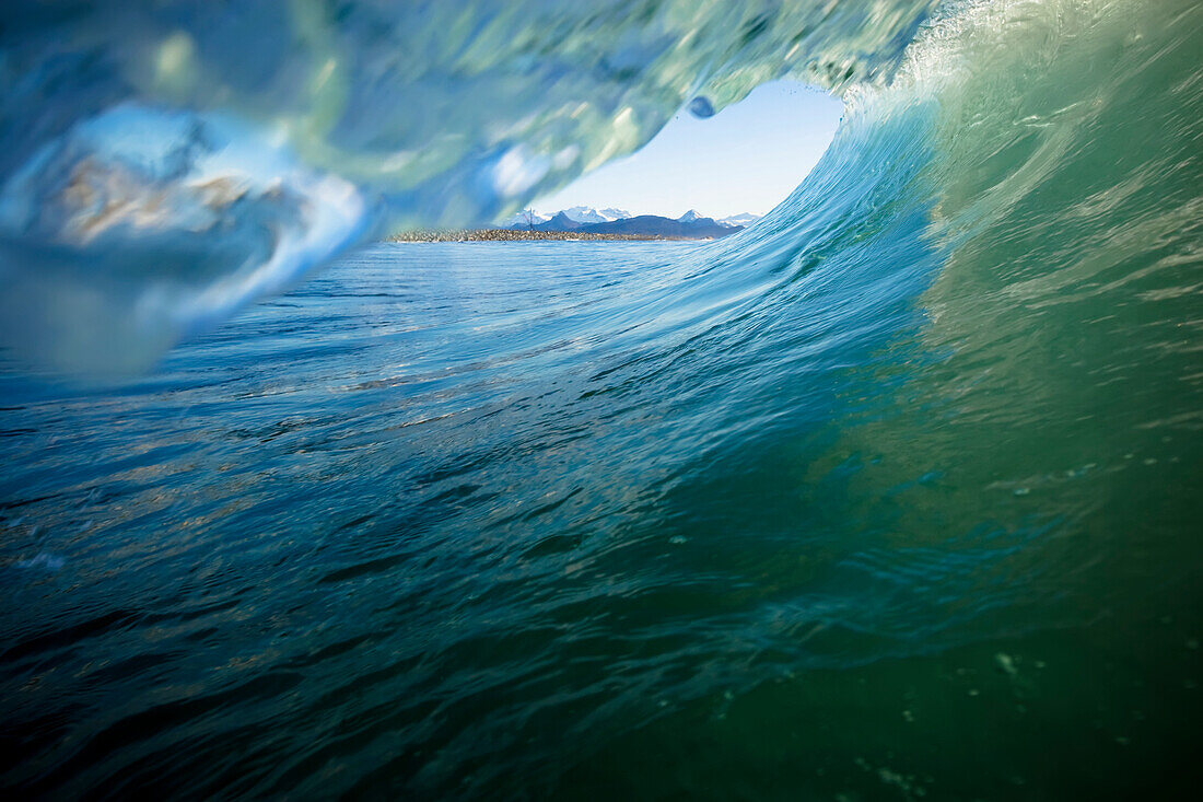 View from inside the barrel of a wave with green and blue ocean water and a view of the mountains, Alaska, United States of America
