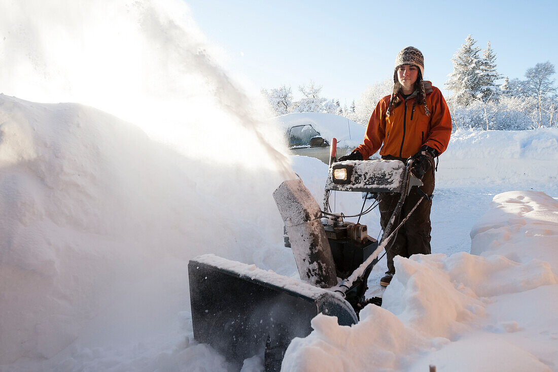 A young woman uses a snowblower in the deep snow, Homer, Alaska, United States of America