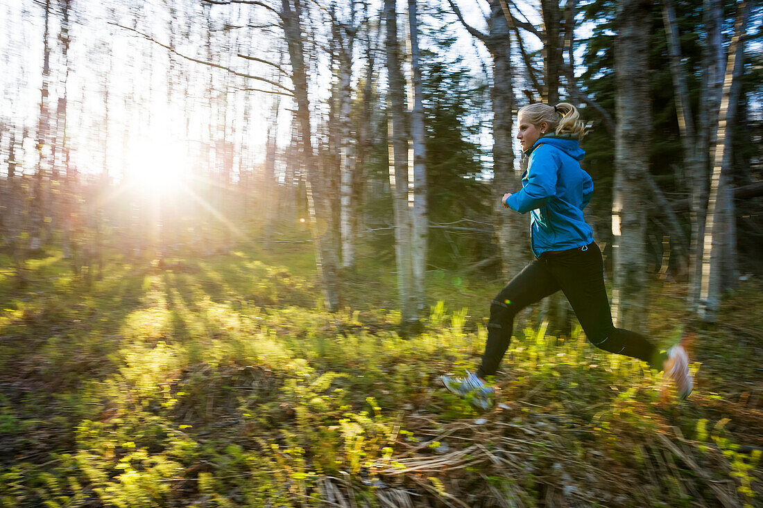 A young woman running across the plants of the forest floor in a forest, Homer, Alaska, United States of America