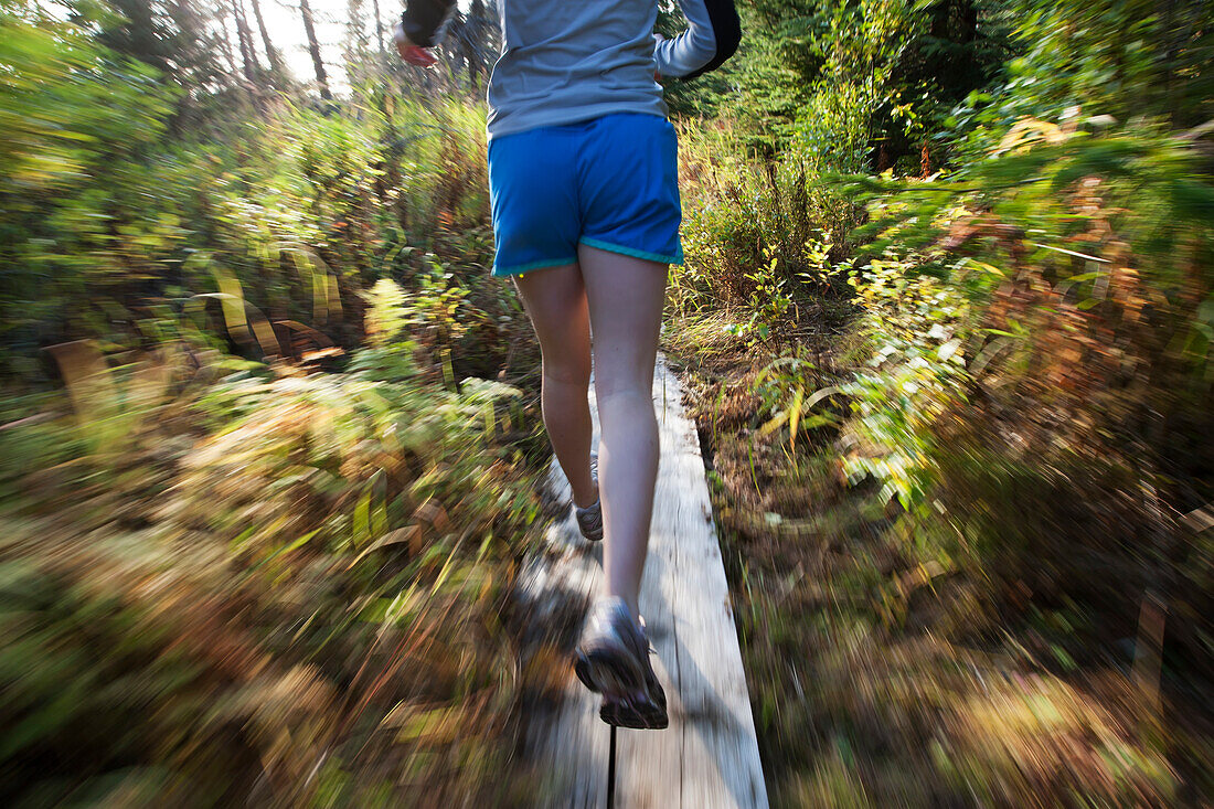 A young woman runs on wooden boards through a forest, Homer, Alaska, United States of America