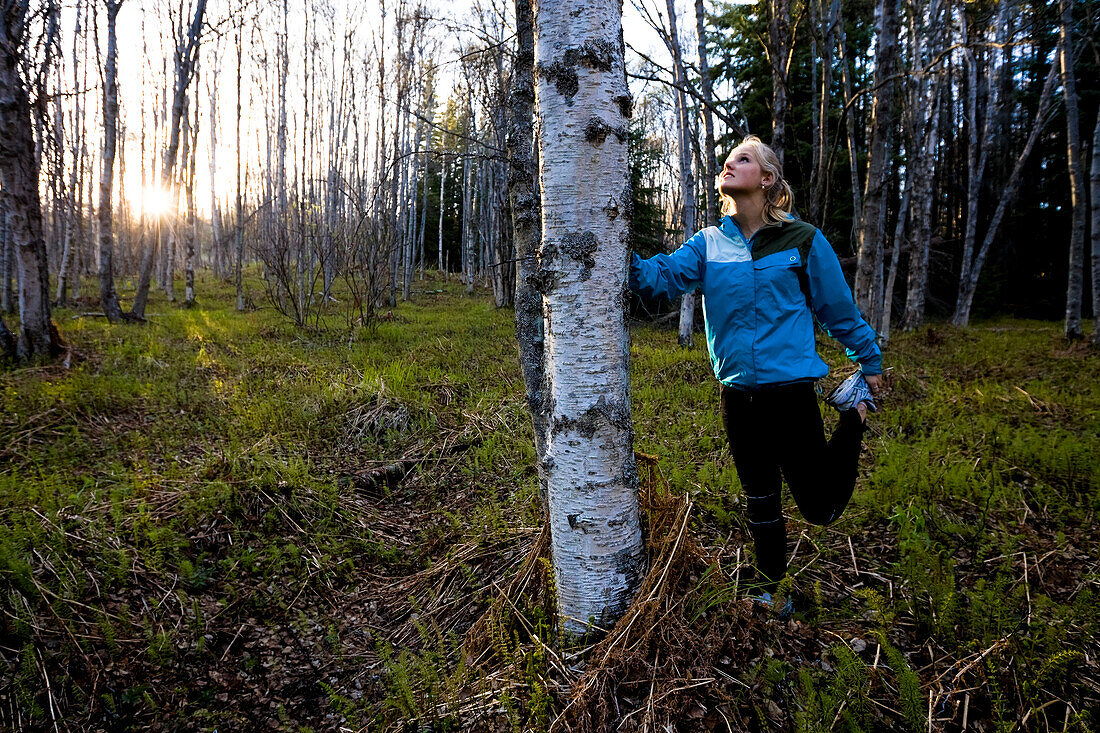 A young woman stretching her legs before a run in a forest, Homer, Alaska, United States of America