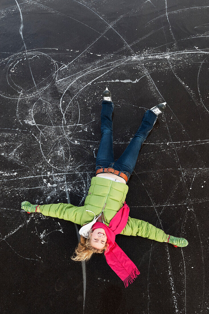 Eine junge Frau legt auf dem Rücken auf eine gefrorene Oberfläche, die beim Eislaufen aufblickt, Alaska, Vereinigte Staaten von Amerika
