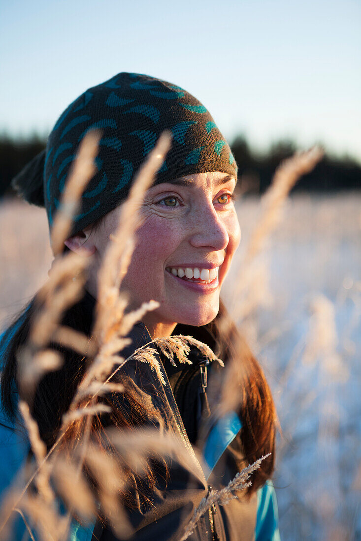 Portrait of a young woman wearing a knit hat and viewed through the tall grasses, Homer, Alaska, United States of America