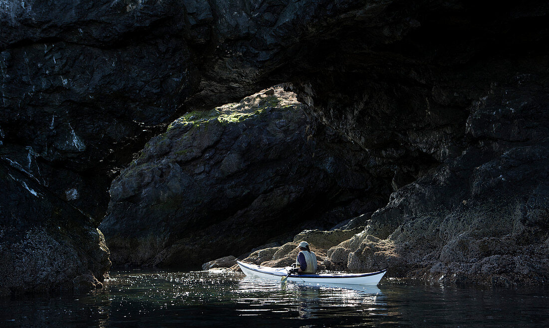 Canoeing along dark rocks of the shoreline in Kachemak Bay State Park, Alaska, United States of America