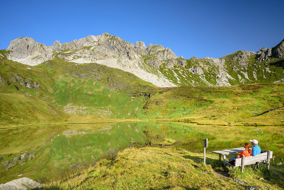 Zwei Personen sitzen auf Bank und blicken auf Iglsee mit Wildkarkopf, Riedingtal, Radstädter Tauern, Niedere Tauern, Kärnten, Österreich
