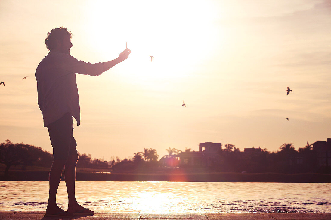 Man using cell phone to photograph sunset