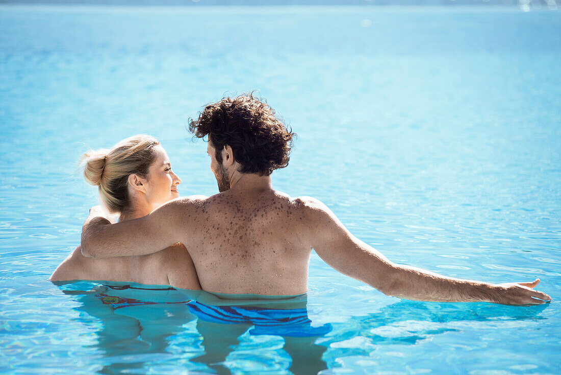 Couple relaxing together in pool, rear view