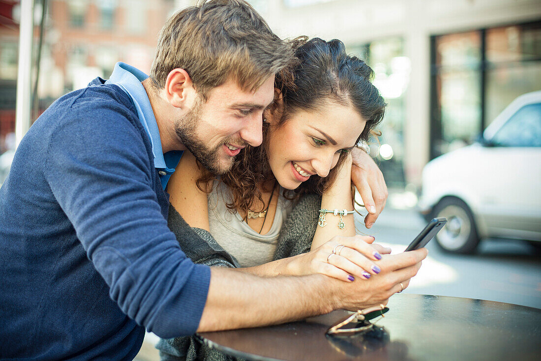 Paar sitzt im Freien zusammen, Blick auf Smartphone
