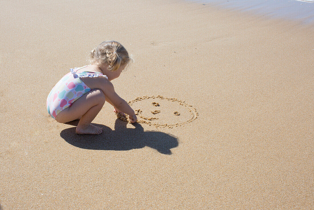 Little girl drawing smiley face in sand