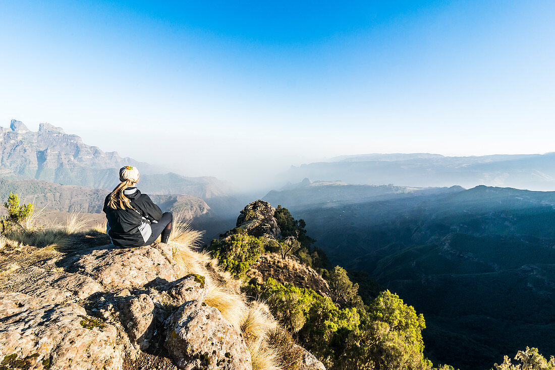Woman enjoying the early morning sun on the cliffs, Simien Mountains National Park, UNESCO World Heritage Site, Debarq, Ethiopia, Africa