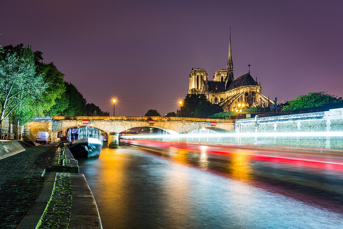Lange Belichtung eines Bootes auf der Seine über Notre Dame Kathedrale an einem nassen Abend in Paris, Frankreich, Europa