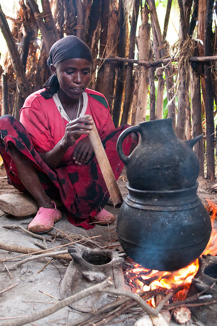 Eine Frau bläst durch eine Holzpfeife, um das Feuer beim Kaffeebrühen auf offenem Feuer, Äthiopien, Afrika