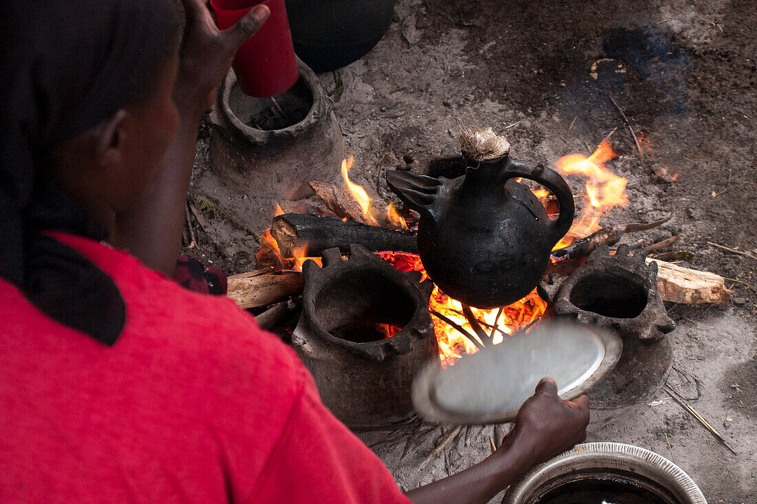 Eine Frau lockt das offene Feuer, als sie Kaffee in einer traditionellen äthiopischen Kaffeekanne, Äthiopien, Afrika