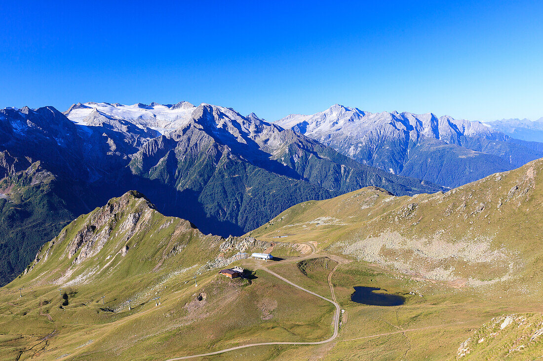 Green meadows and alpine lake framed by the high peaks in the Adamello Ski Area, Tonale Pass, Valcamonica, Lombardy, Italy, Europe