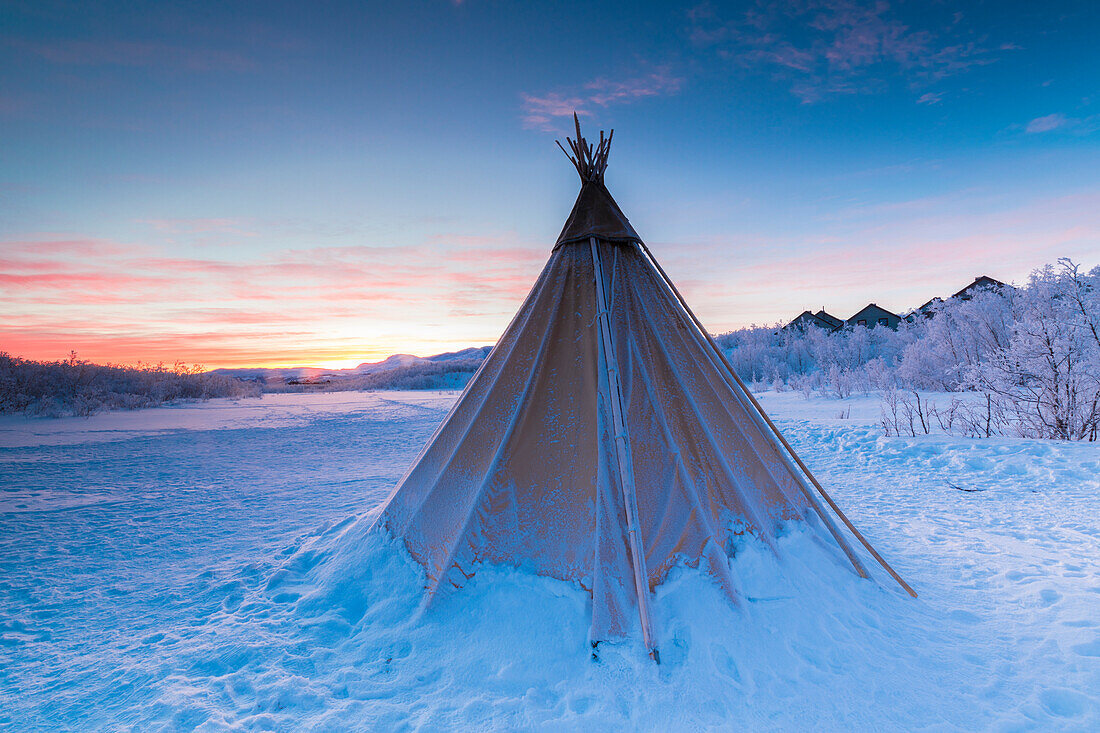 Pink sky at sunrise on isolated Sami tent in the snow, Abisko, Kiruna Municipality, Norrbotten County, Lapland, Sweden