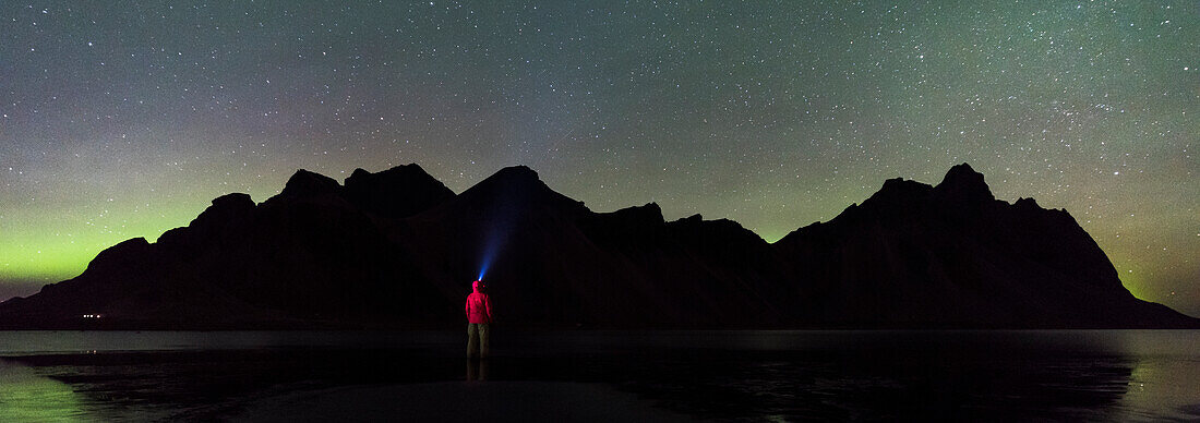 Stokksnes, Hofn, Eastern Iceland, Iceland, One man standing on the beach at night gazing at the northern lights and Vestrahorn mountain