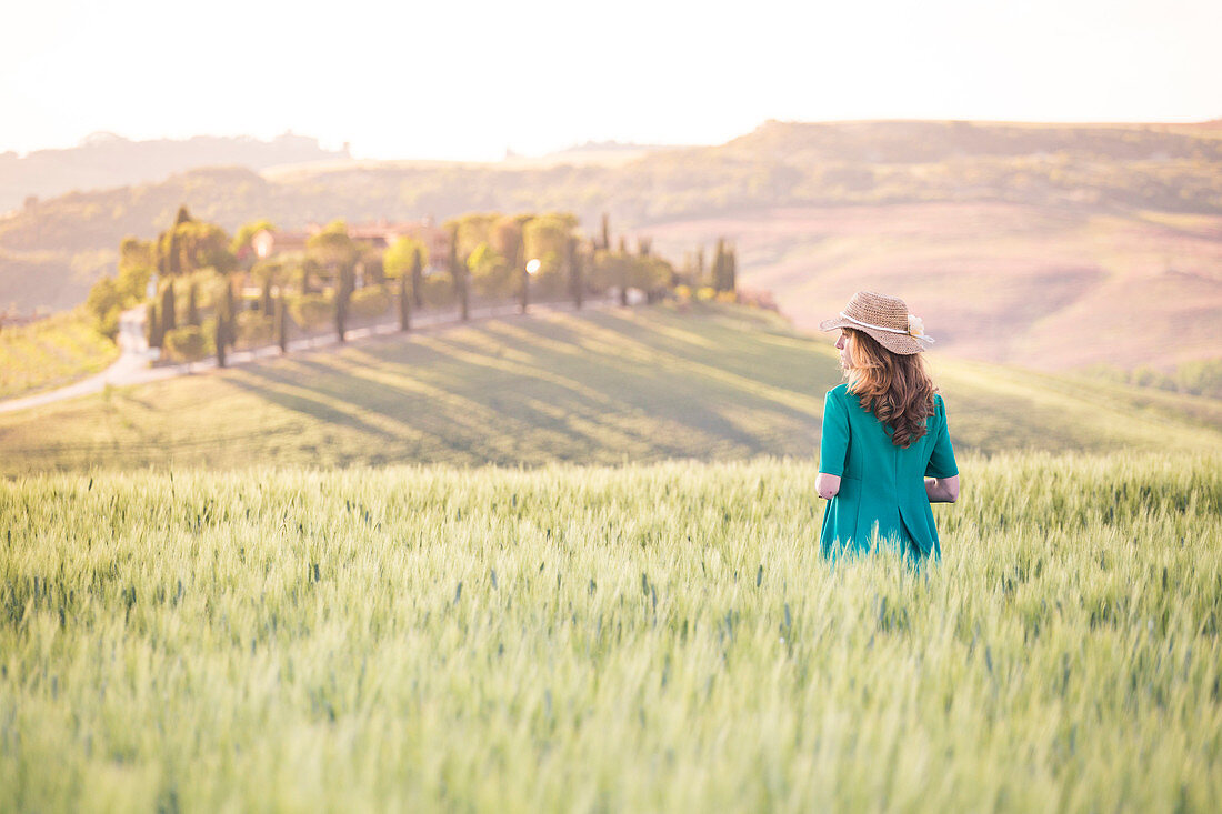 A girl in a green dress walking trough the golden fields of Tuscany, Val d'Orcia, Province of Siena, Tuscany, Italy