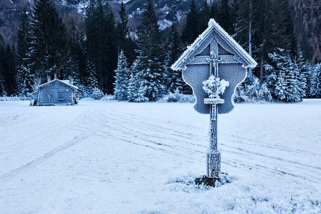 Europa, Italien, Venetien, Belluno. Eine hölzerne Hütte und ein Kruzifix mit Eis bedeckt im Ansiei-Tal im Winter, Auronzo di Cadore, Dolomiten