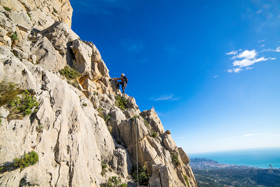 Ein Mann Klettern hoch auf dem Gipfel des Puig Campana über der Stadt Benidorm, Alicante Region, Costa Blanca im Mittelmeer Spanien.