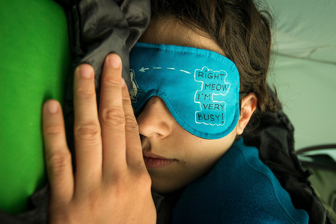 Portrait of woman sleeping with eye mask with funny message in a tent. She's sleeping on her stomach, on arm in front of her face, only half of the face is visible.