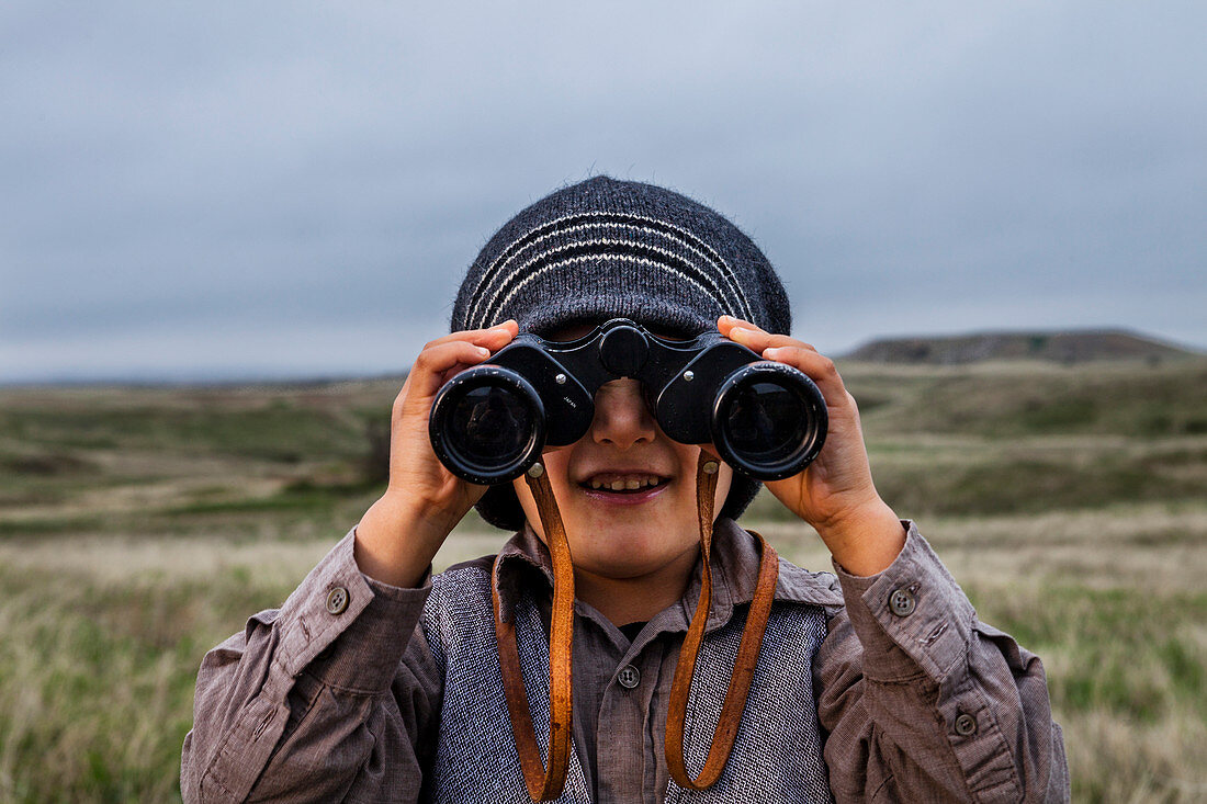 Ein 4-jähriger japanisch-amerikanischer Junge, der als Forscher mit Hut und Weste gekleidet ist, untersucht das Land (Grasland und Prärie) mit seinem Fernglas im Badlands National Park in South Dakota.