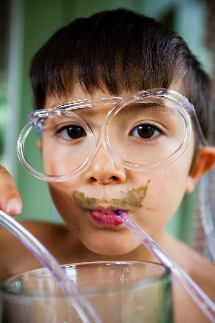Ein 6-jähriger japanisch-amerikanischer Junge trinkt Grüns aus seiner seltsamen Strohbrille.