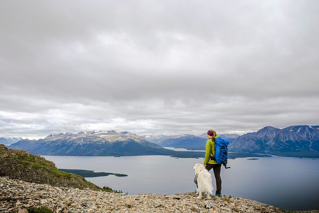Female hiker with dog on Monarch Mountain overlooking Atlin Lake towards the Boundary Mountain Ranges British Columbia