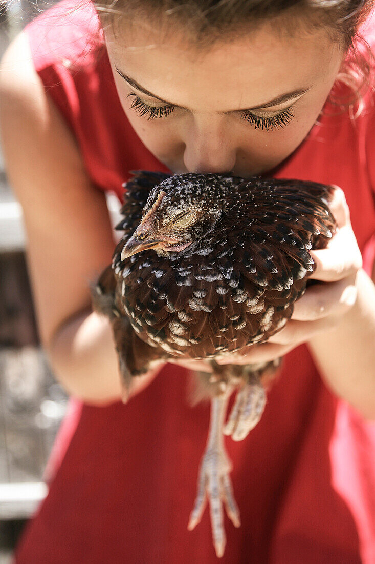 Young Woman in a red dress holds and kisses a chicken affectionately.