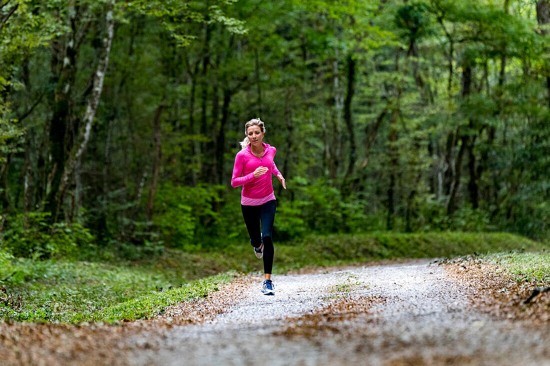 Frau trägt eine rosa Spitze und läuft allein auf einer Straße in einem grünen Wald im Herbst, in der Nähe von Eloise, Frankreich