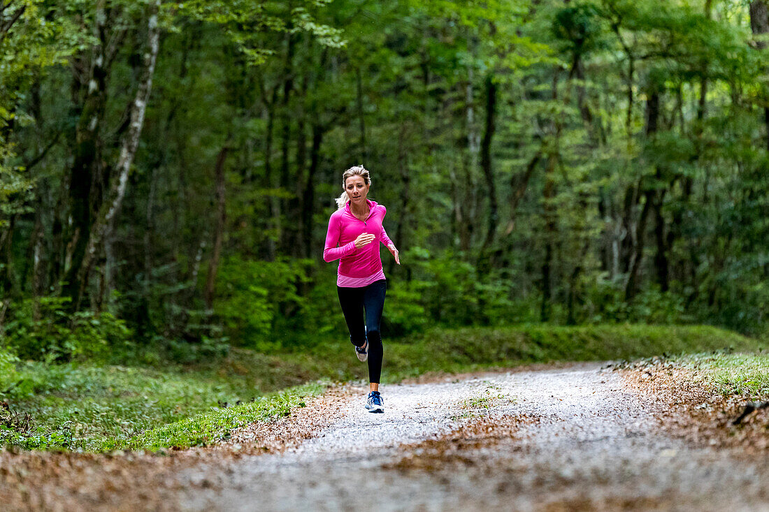woman wearing a pink top and running alone on a road in a green forest in Autumn, close to Eloise, France