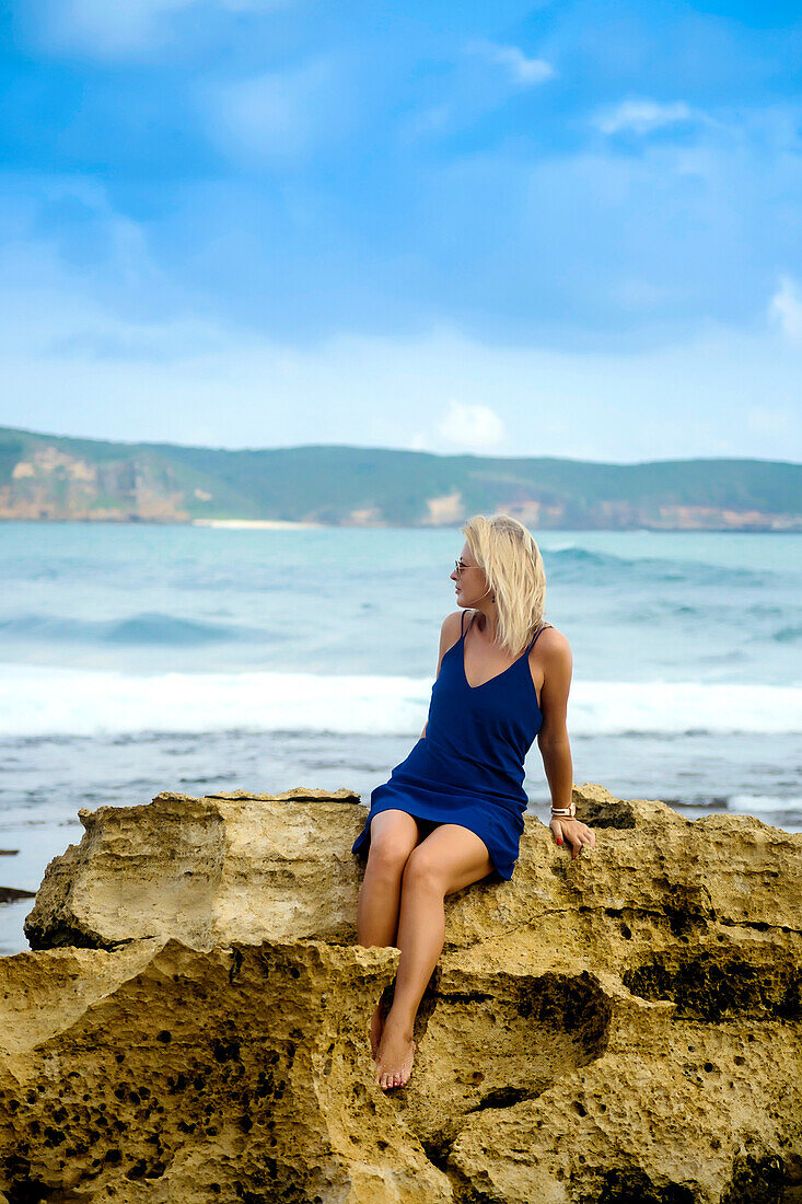 Frau im blauen Kleid sitzt an der Küste, Betrachtung