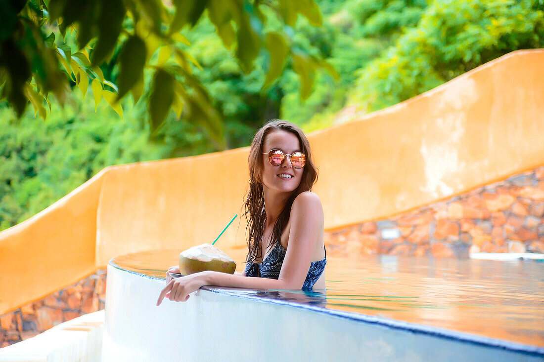 Woman sitting on edge of infinity pool with coconut water