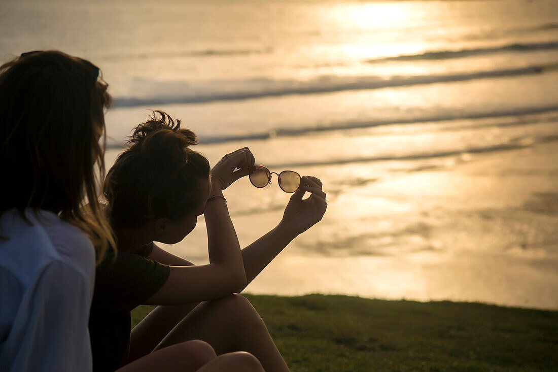 Two women sitting on beach at sunset