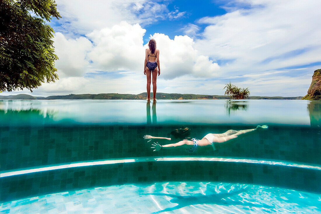 Young woman swimming in outdoor swimming pool beside woman standing outside