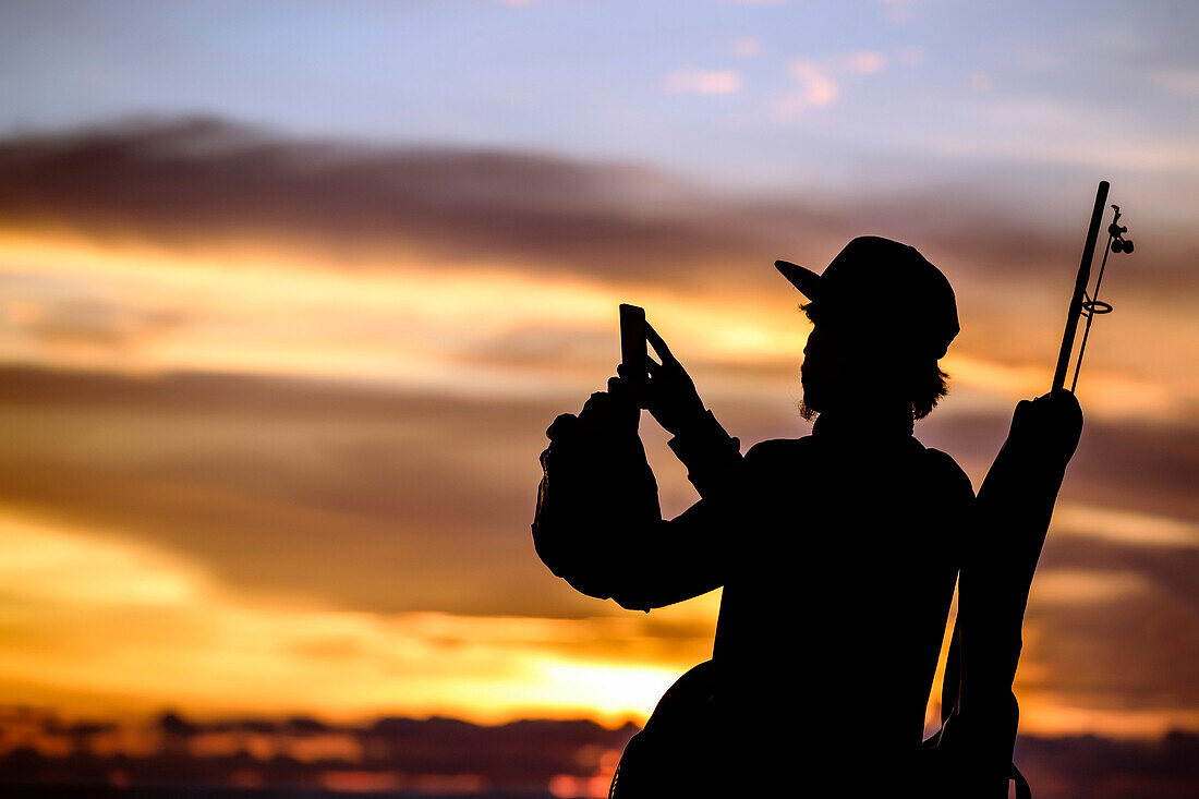 Silhouette of fisherman taking picture with smartphone at sunset