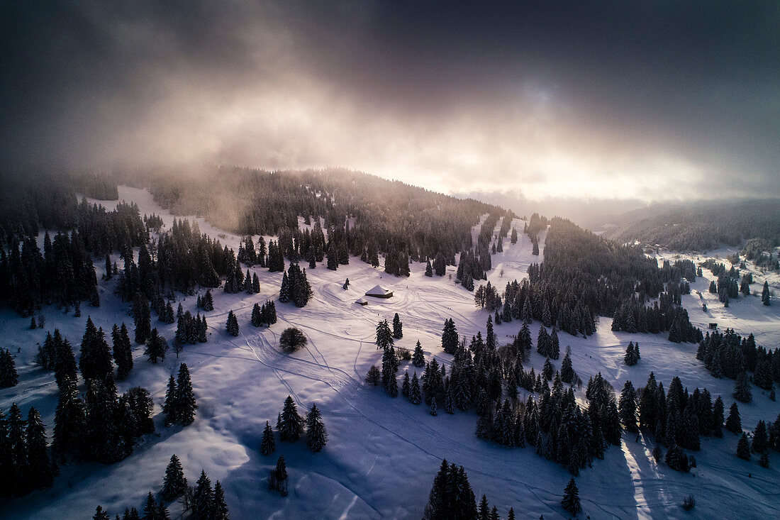 aerial view of sunrise on Jura mountains with spruce's (Picea Abies) shadow and mountain refuges with wonderful lights and clouds in the sky in Vaud Canton, Switzerland