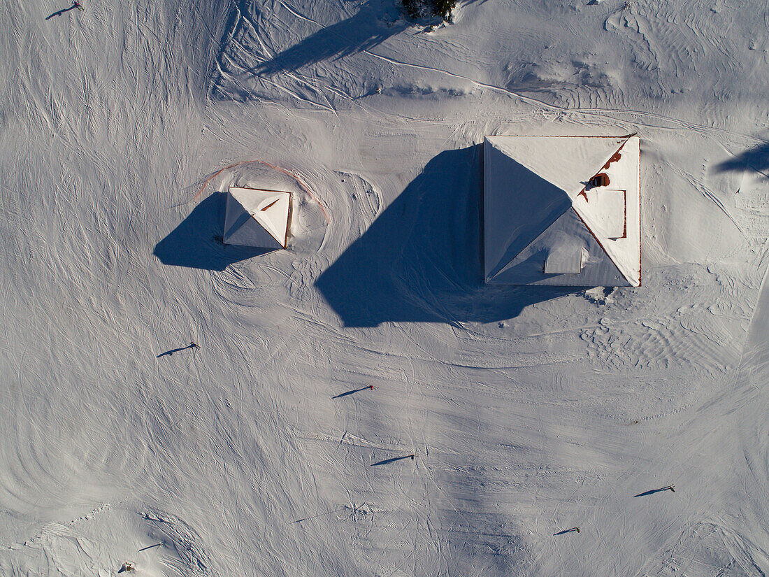 aerial view of a snowy landscape showing roofs of mountain refuges with skiers around on a sunny day in Vaud Canton, Jura mountains, Switzerland