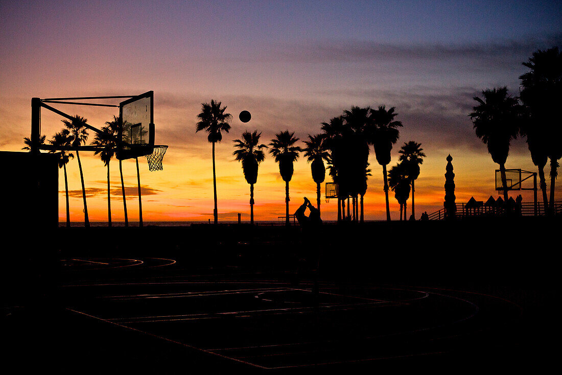 Silhouetten von Palmen und Basketball Hoop am Santa Monica Strand während des Sonnenuntergangs, Kalifornien, USA