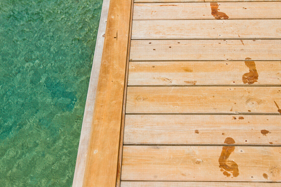 Nasse Fußabdrücke verfolgen auf hölzernem Pier nahe bei Meer, West End, Roatan, Honduras